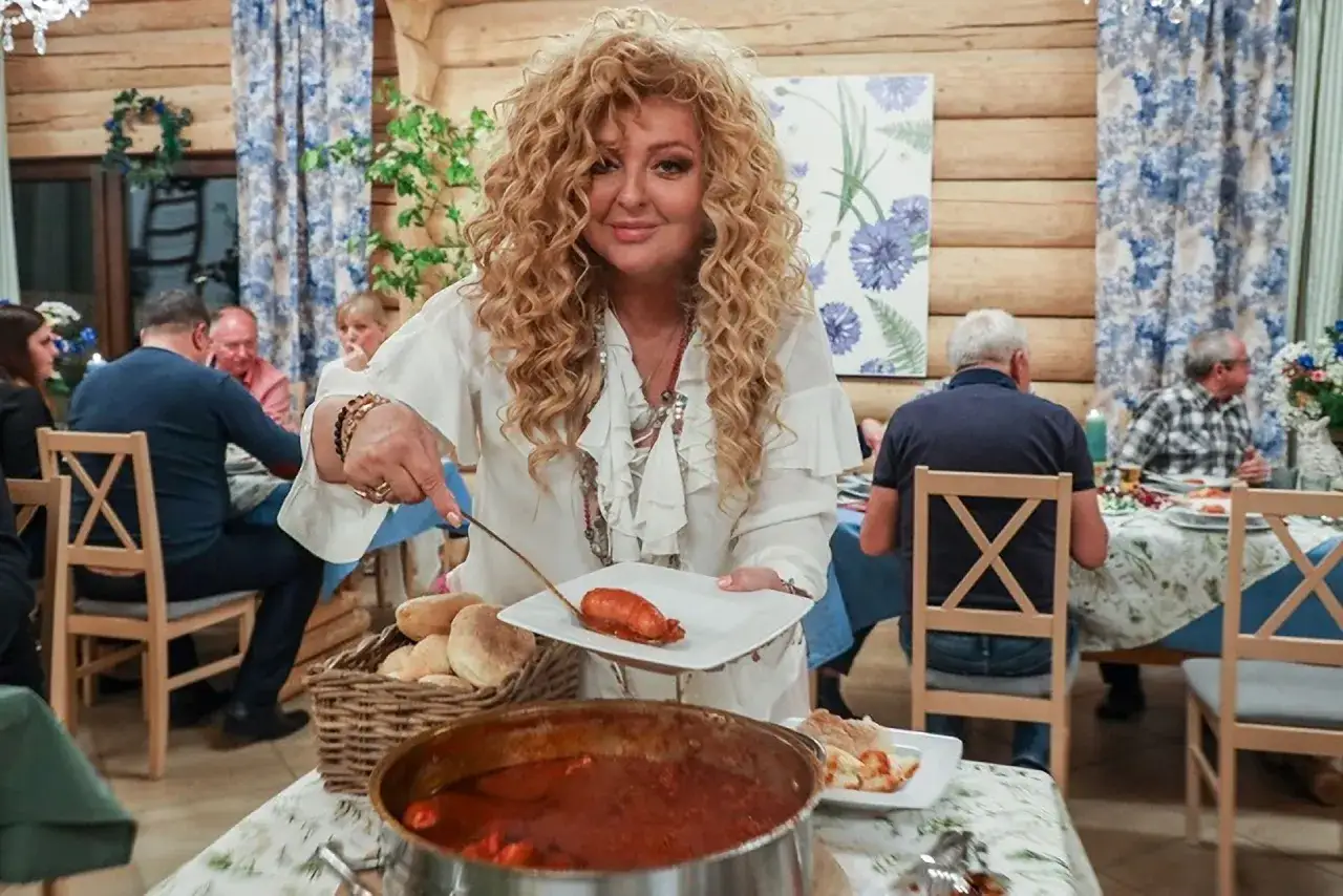 Kobieta z burzą blond loków nakłada kiełbaskę na talerz. Wszyscy czekają, aż do stołu marsz.