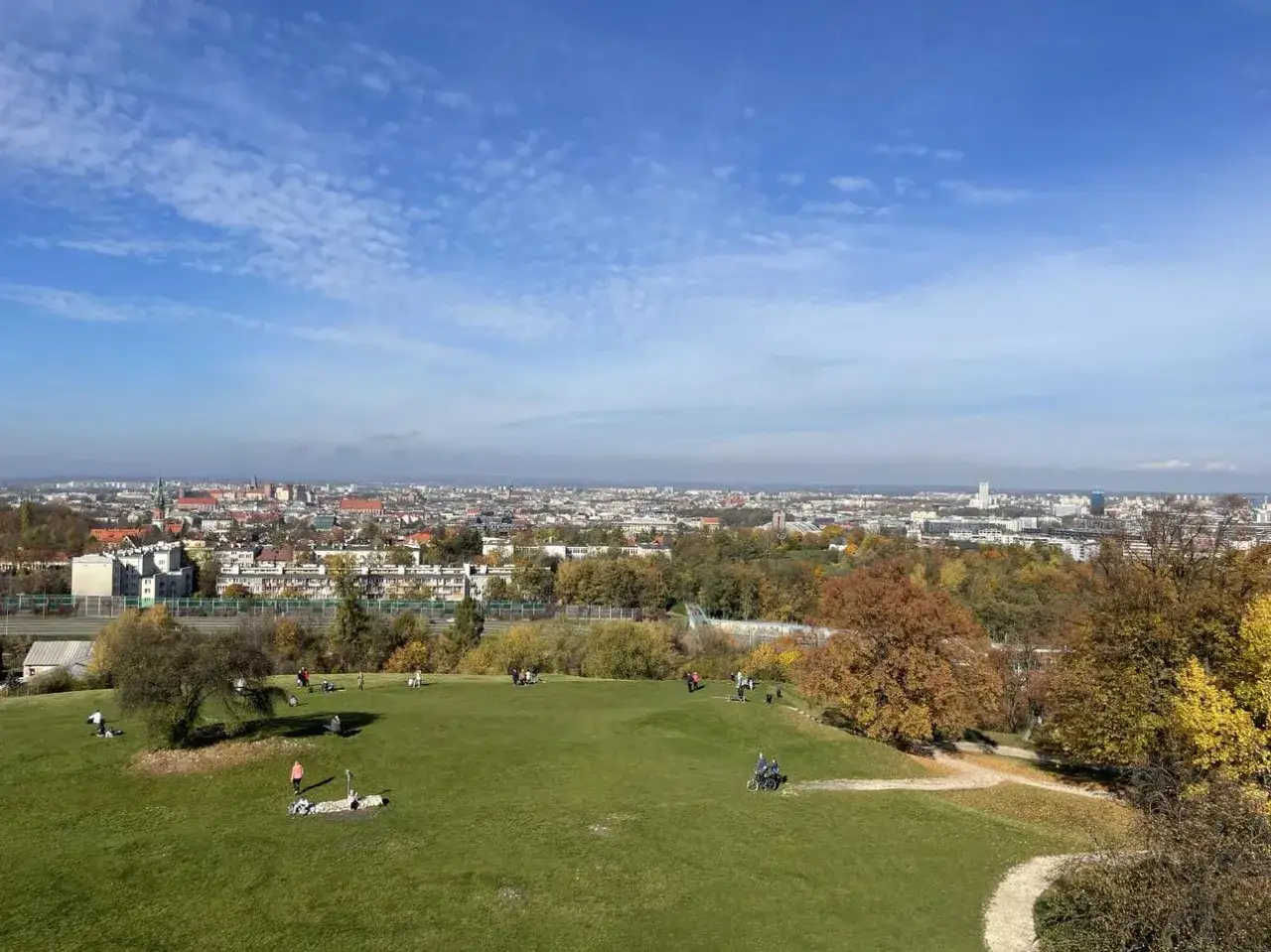 Jesień na Kopcu Kraka w Krakowie. Ludzie odpoczywają na trawie, w tle rozciąga się panorama miasta.