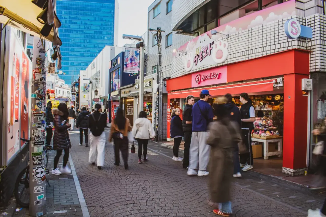 Tętniąca życiem Takeshita Street w Tokio, pełna sklepów z pluszakami i kolorowych fasad. Ludzie spacerują po brukowanej ulicy, chłonąc atmosferę.