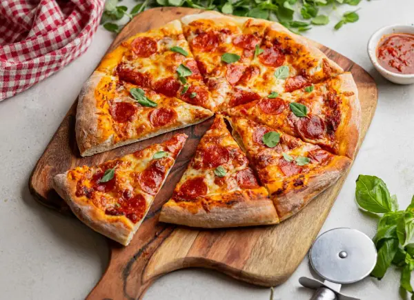 Krojona pizza pepperoni z serem i bazylią na drewnianej desce.